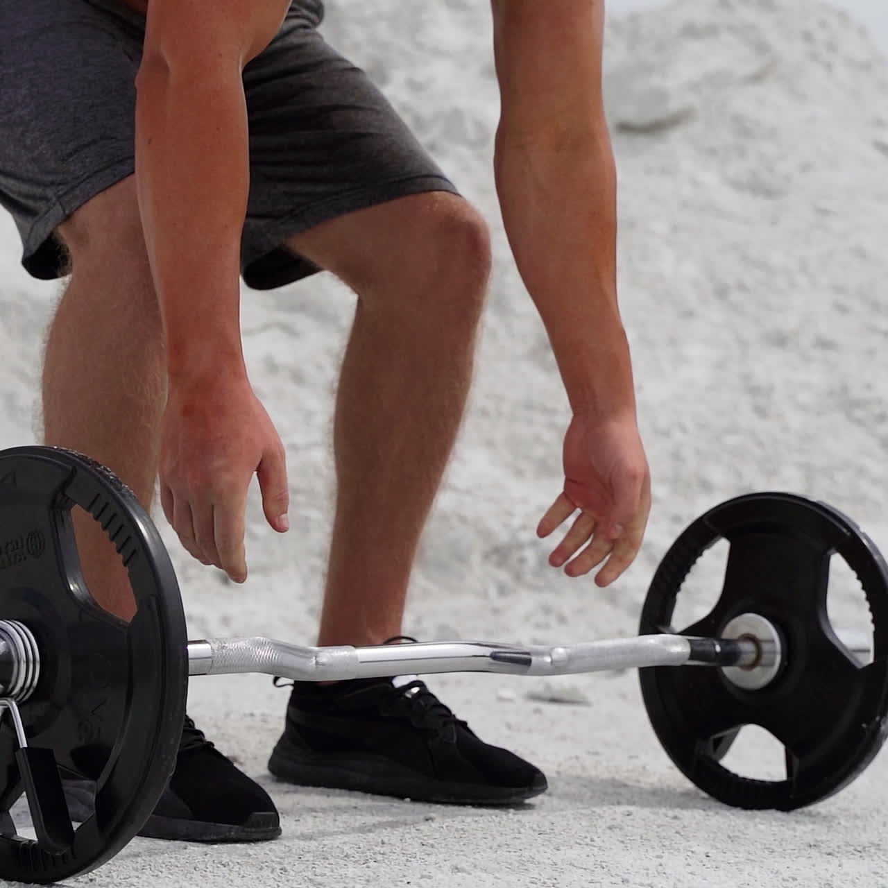Close-up view of muscular man's body with barbell outdoors. Bodybuilder is doing his workout on the white mountain background.