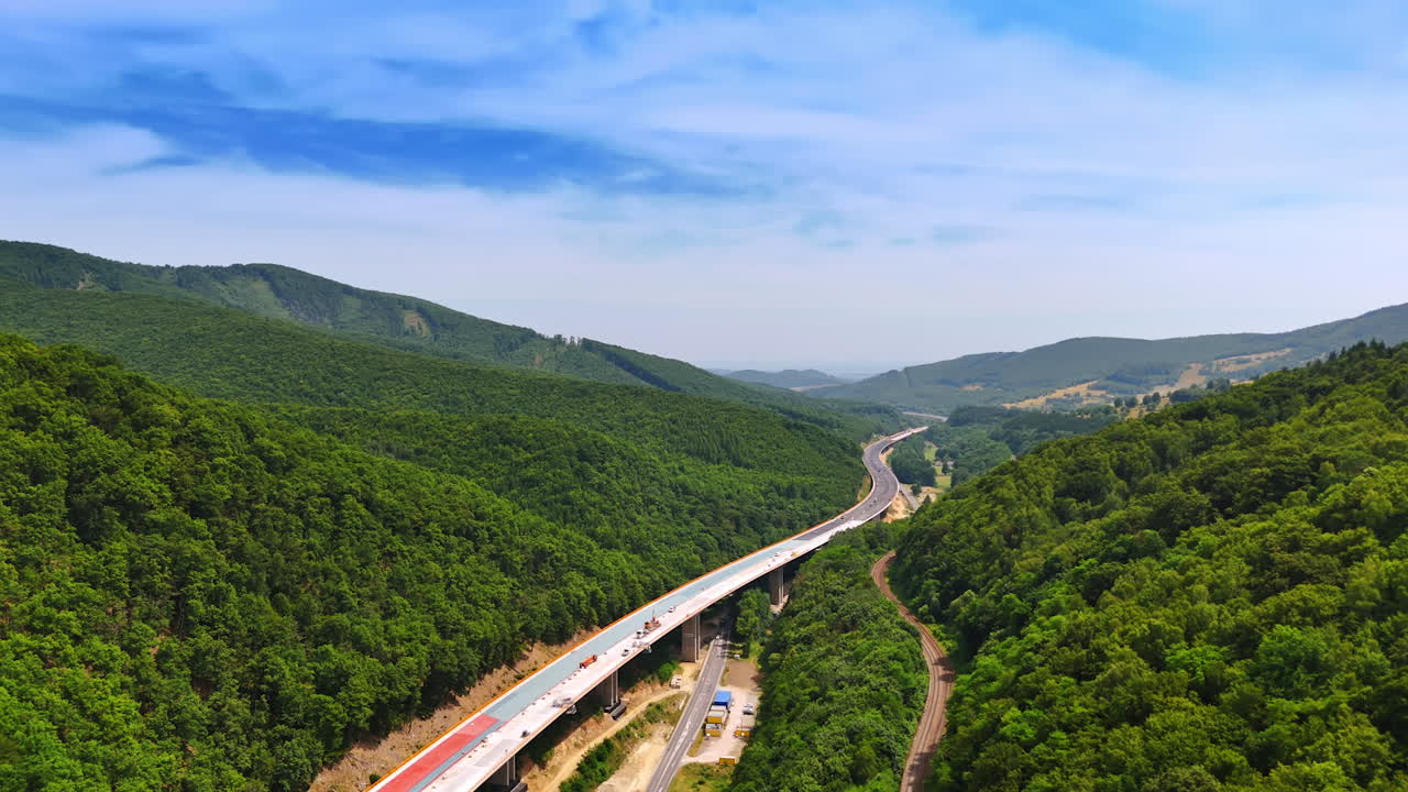 Construction of a new freeway in the spectacular wooded mountains. Building of the road above the old highways. Aerial view