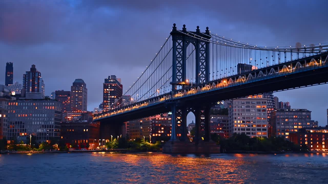 Il Manhattan Bridge e lo skyline di New York con i lampioni accesi di sera. Angolazione dal basso sul ponte dal paesaggio fluviale