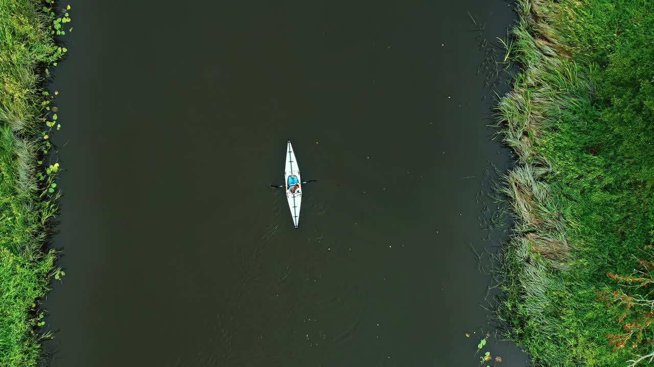 Single person kayaking in a narrow river, top-down view of foldable boat in nature