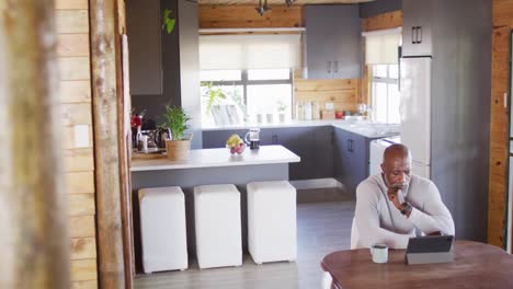 senior african american man in log cabin, sitting at table and using tablet, slow motion