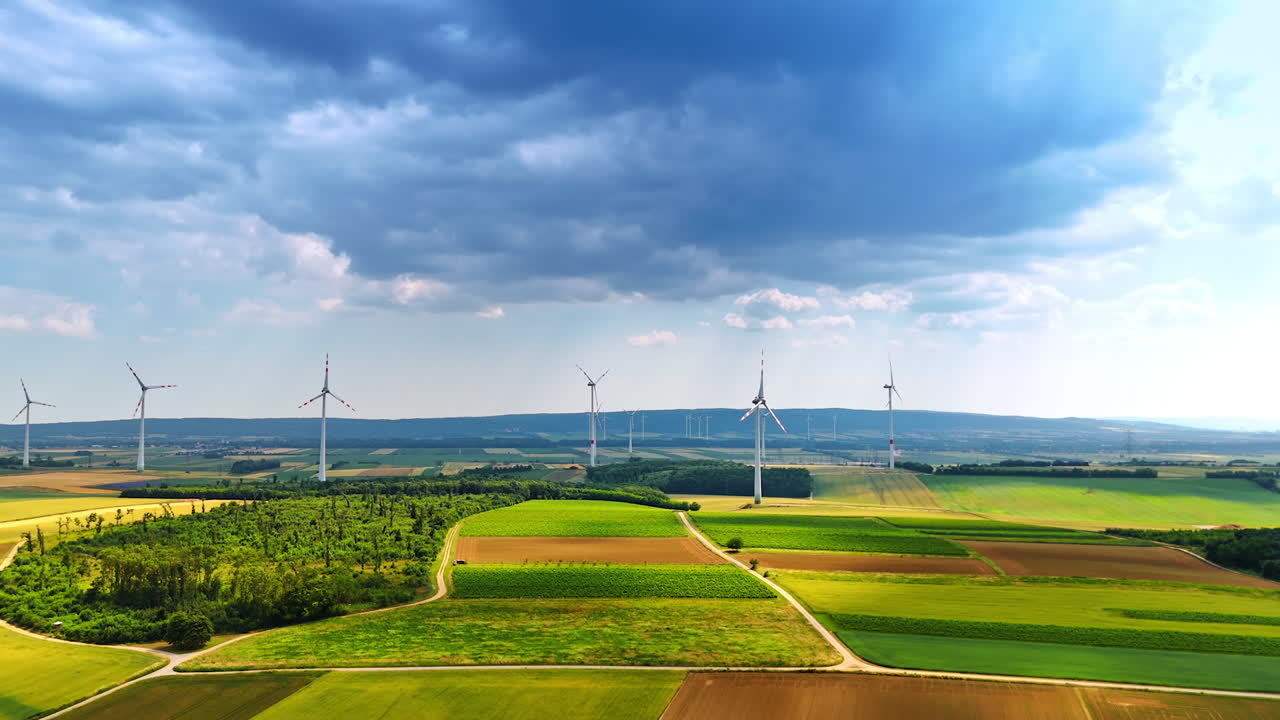 Picturesque fields under the rainy cloudscape. Lots of wind mills rotate in the wind. Aerial view