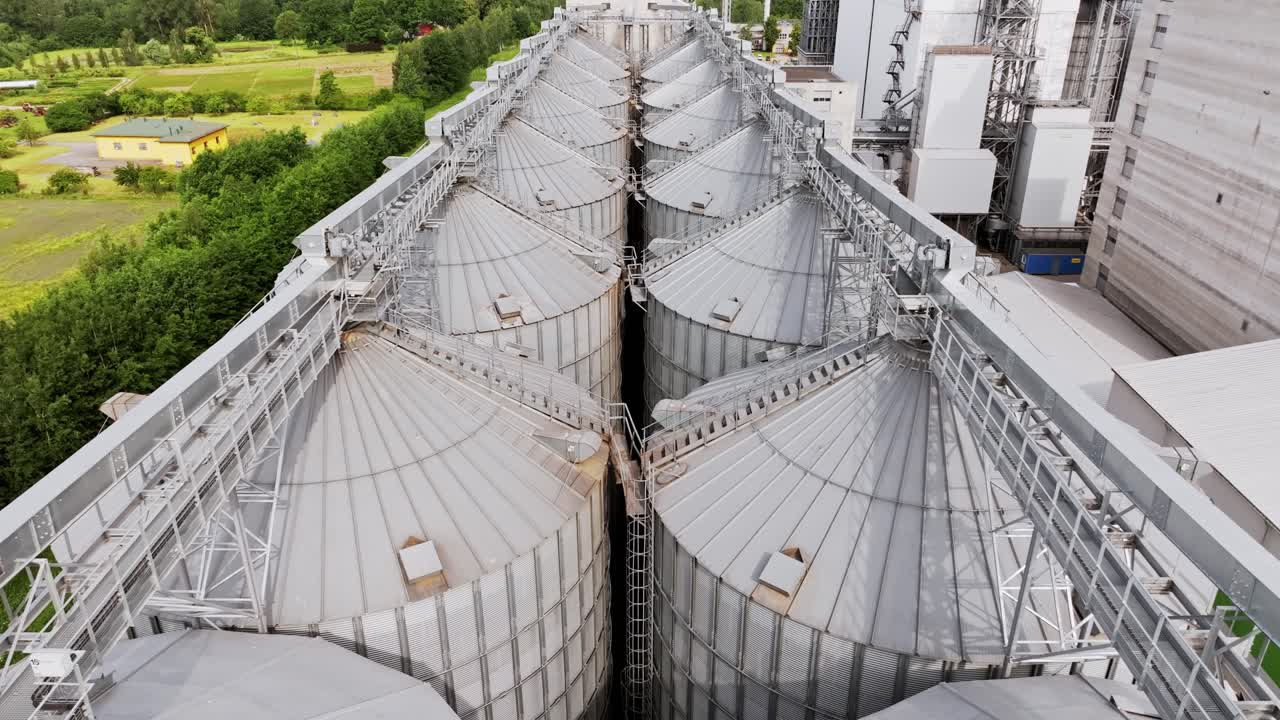 Industrial grain tanks framed by greenery and fields in scenic drone view