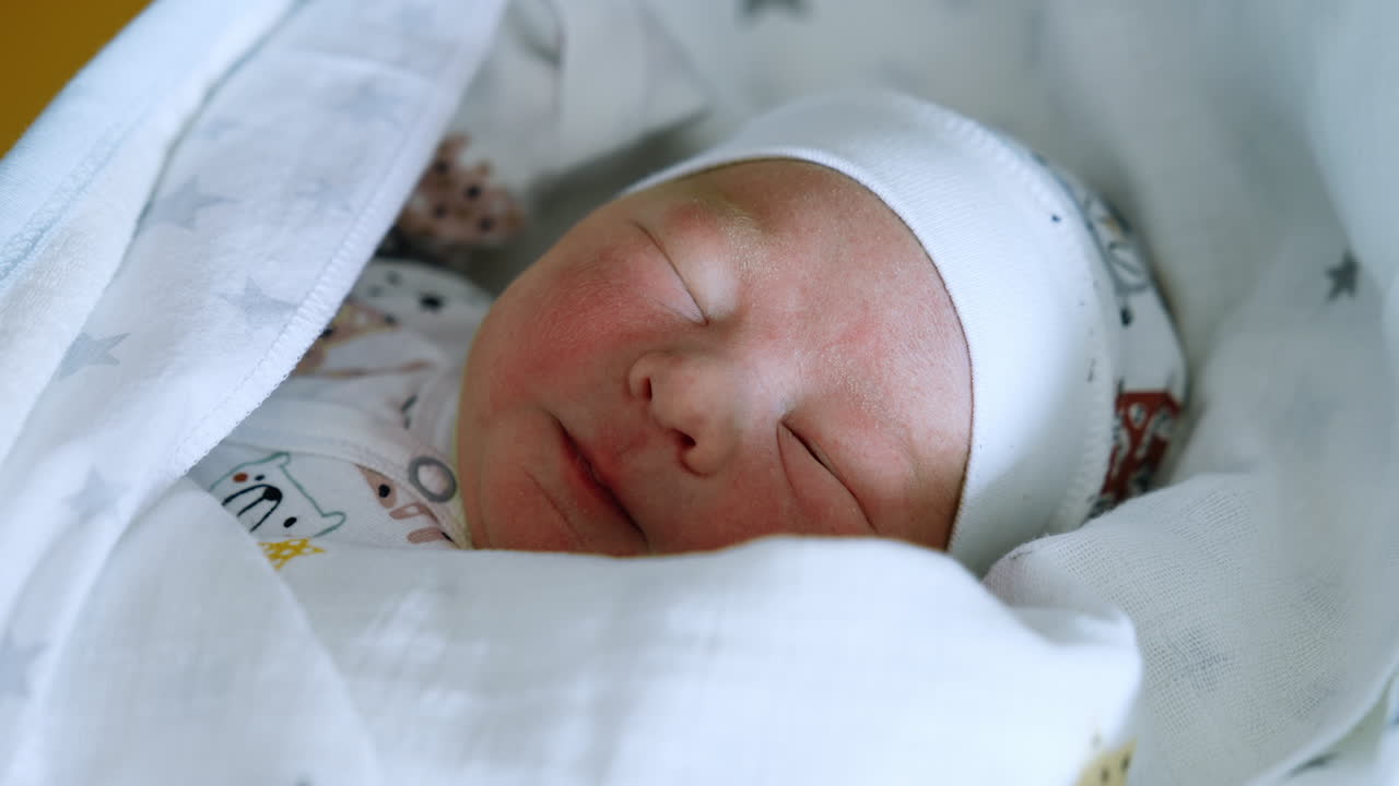 Adorable newborn Caucasian child wakes up and makes faces. Baby opens one eye and falls asleep again. Close up.