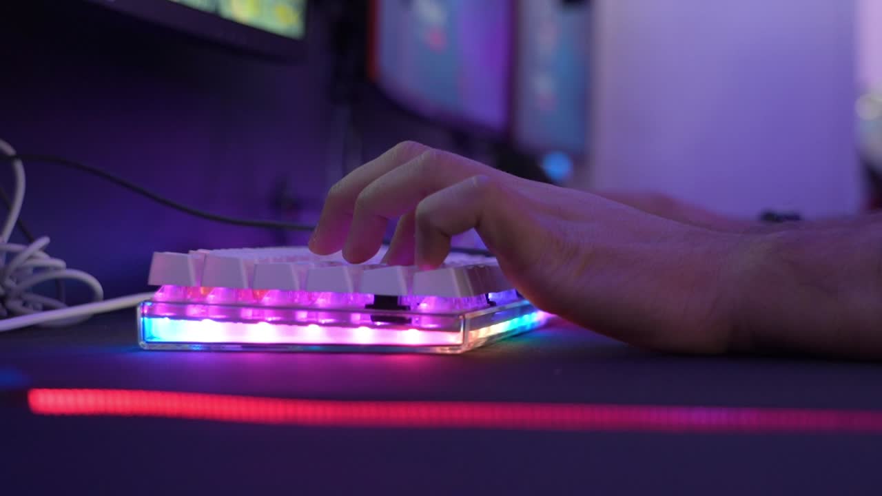 Close up of the hand of a human playing pc games on a led multicolored keyboard in an internet cafe