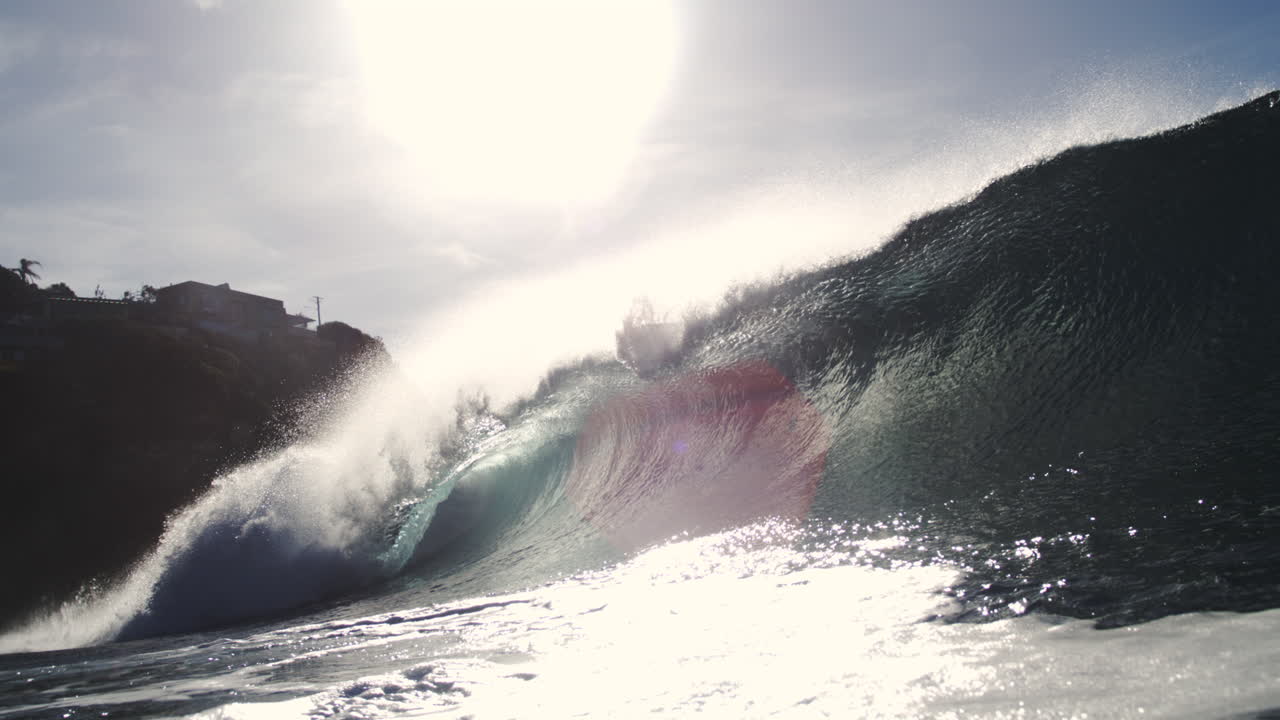 Glassy wave crashes in slow motion with shimmering backlight