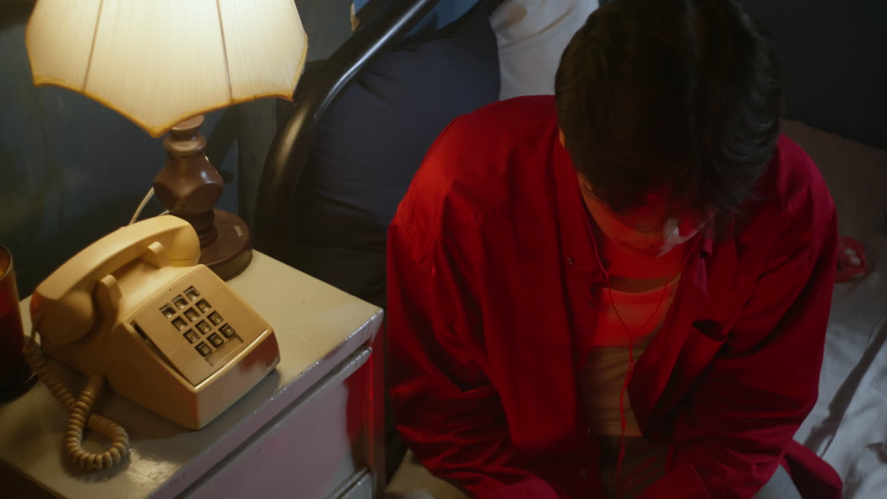 침대  램프와 빈티지 전화로 호텔 방에 앉아 오래된 카세트 플레이어를 듣고 있는 외로운 남성