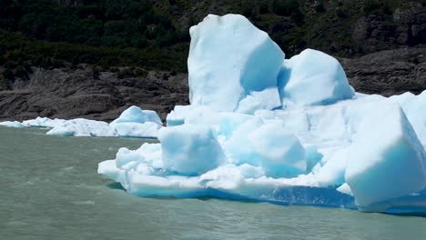 melting iceberg floating along grey lake, slow motion