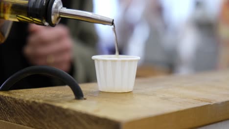 Close-up-slow-motion-of-whiskey-being-poured-into-paper-cup-for-tasting-at-local-summer-market-fair