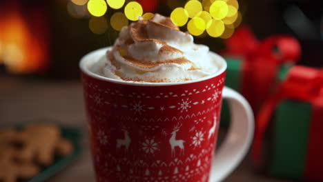 sprinkling cinnamon over whipped cream in a red cup filled with hot chocolate, christmas dessert by the fireplace