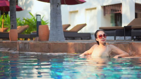 joven asiática con grandes gafas de sol se relaja en la piscina del complejo