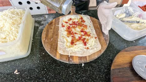 adding toppings to pizza dough on wooden board