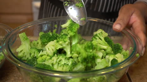 cook stirs steamed broccoli in glass bowl with tablespoon, slow motion