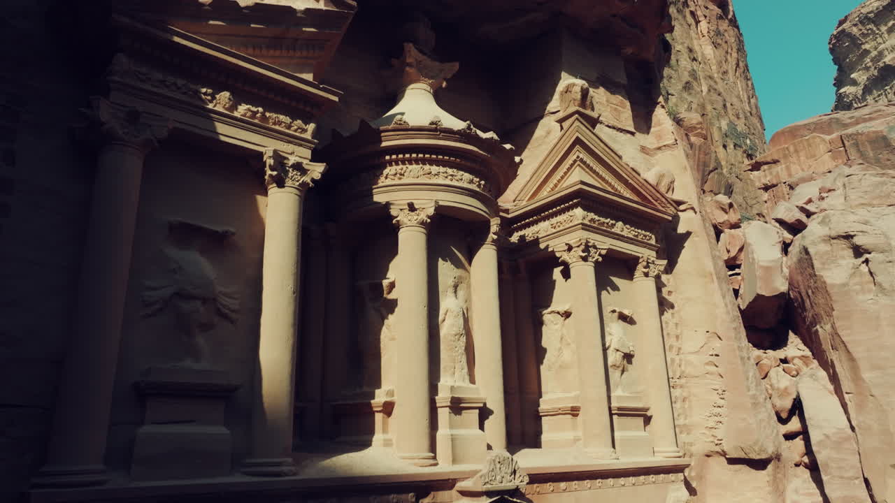 atracción turística popular la tumba del tesoro esculturas cortadas en roca con luz solar que destacan detalles arquitectónicos, drones que ascienden