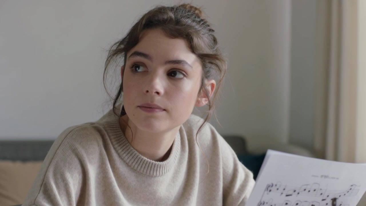 Studentessa che si esercita a casa, sistemando lo spartito sul leggio, sentendo bussare e girando la testa