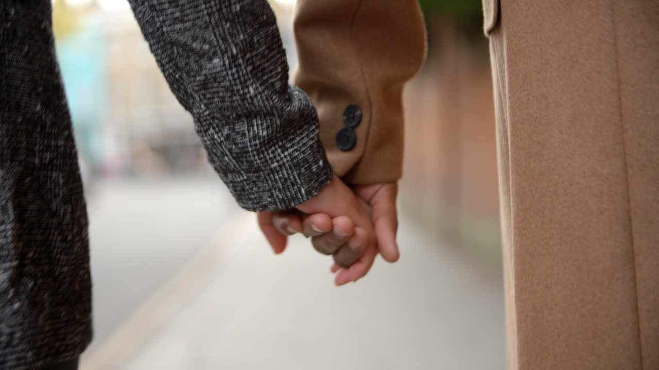 Close Up Of Couple Holding Hands Walking Along City Street