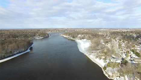 Aerial-view-of-a-river-flowing-through-a-town,-with-melting-snow,-on-a-sunny-day