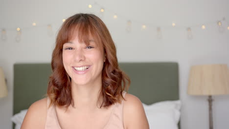 biracial young woman smiling at camera in bedroom at home, copy space