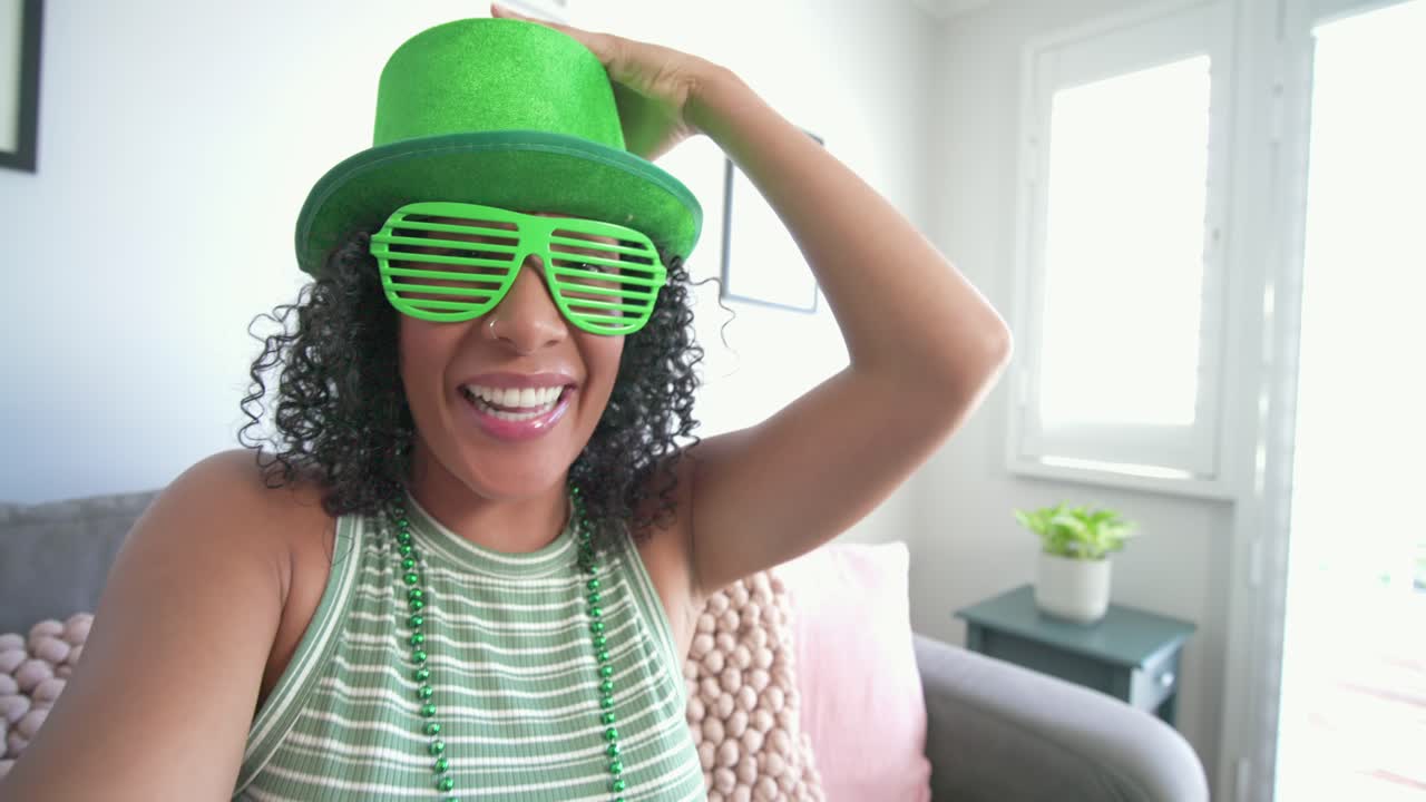 African American woman adjusting green slatted sunglasses grabbing hat on living room sofa posing