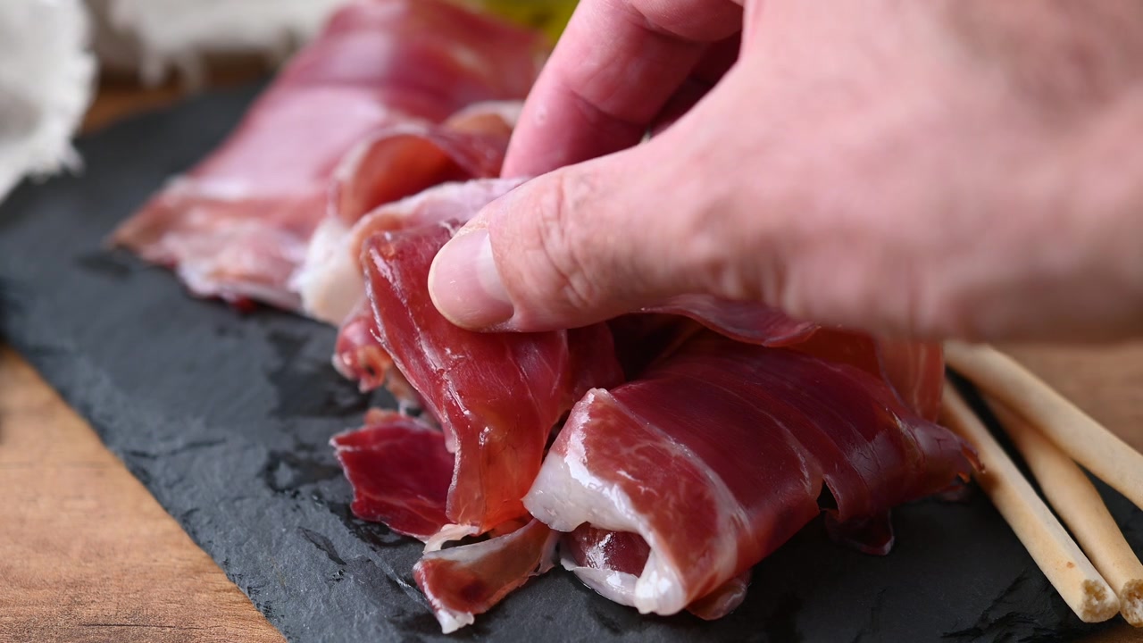 Mano che prende una fetta di jamón spagnolo affettato sottilmente