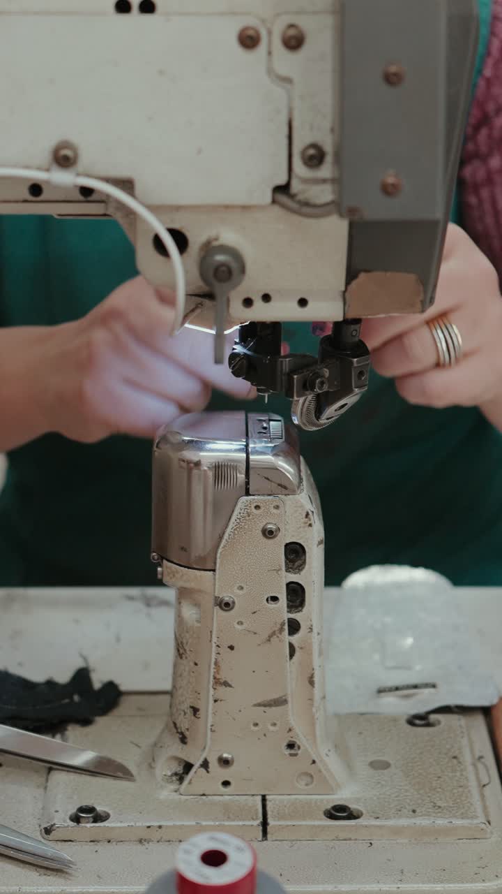 Vertical closeup of worker inserting thread into needle of footwear sewing machine