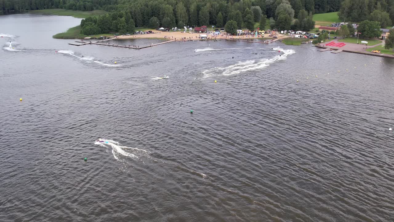 Multiple jet skis ride swiftly across the surface of a lake, creating ripples and waves in the water. The scene captures the excitement of water sports on a calm lake.