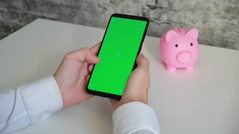 teléfono con pantalla verde y alcancía en fondo blanco vista superior. teléfono inteligente chromakey desliza en diferentes direcciones. copia espacio
