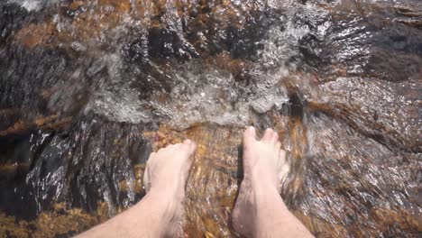 male dipping toes in river water over whitewater rocks, closeup