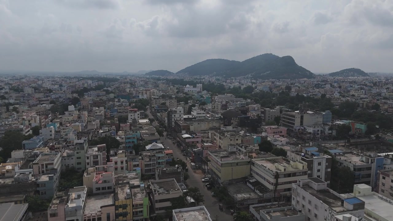 Veduta aerea con drone della città di Vijayawada, dove le strutture urbane si fondono con il paesaggio verde e la collina in lontananza.
