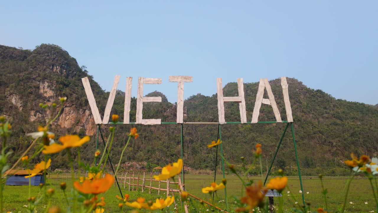 Viet Hai Sign In The Field With Mountains And Yellow Flowers In Cat Ba Island, Vietnam. - wide shot