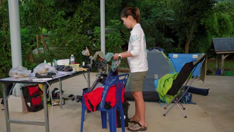 Shot-of-a-young-woman-packing-up-her-backpack-after-camping-trip-in-Pak-Nai-fisherman-village,-Nan-province,-Thailand