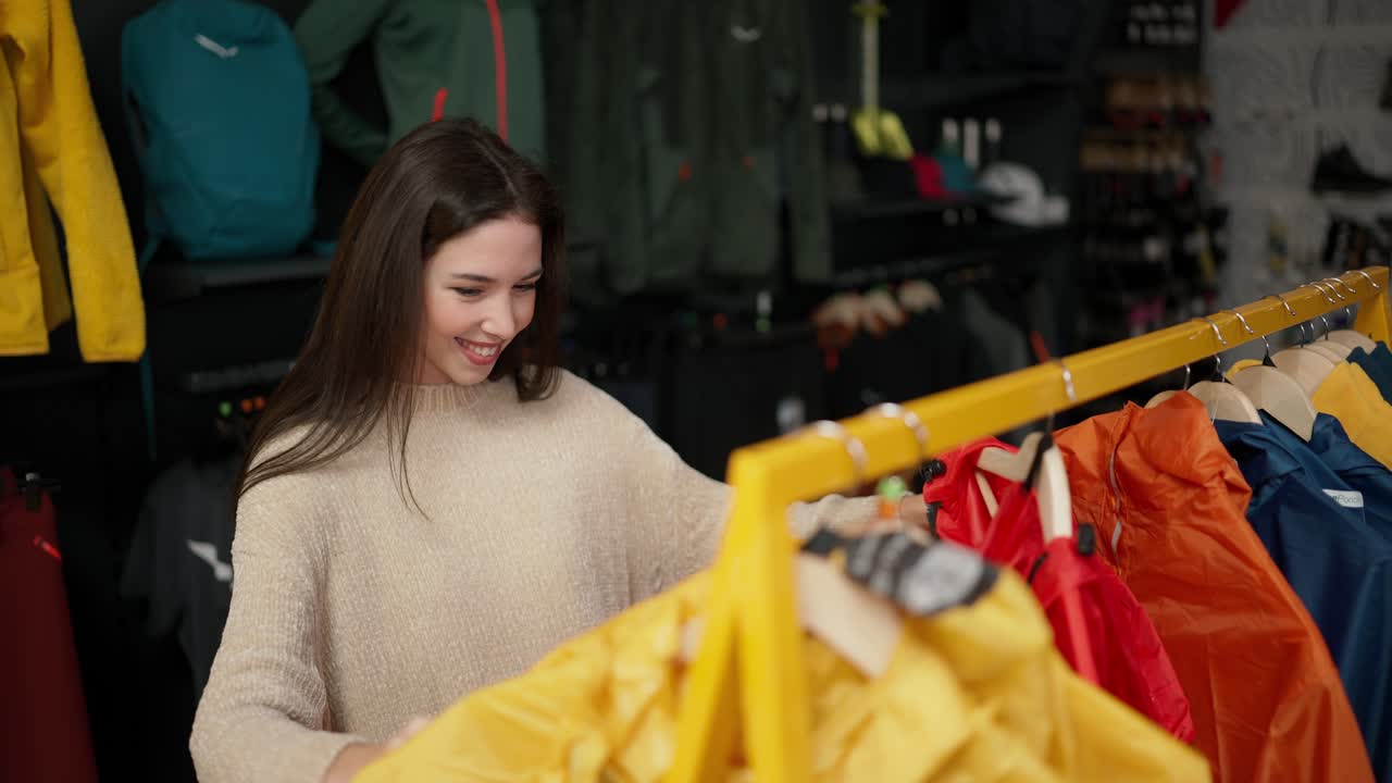 Una donna che fa shopping nel centro commerciale, scegliendo abbigliamento sportivo su un espositore.