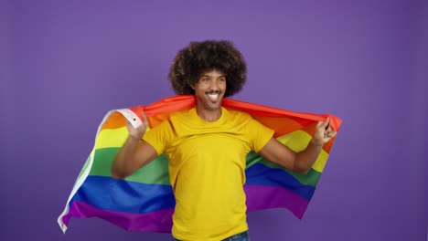 smiling man with afro wrapped in rainbow pride flag against purple background