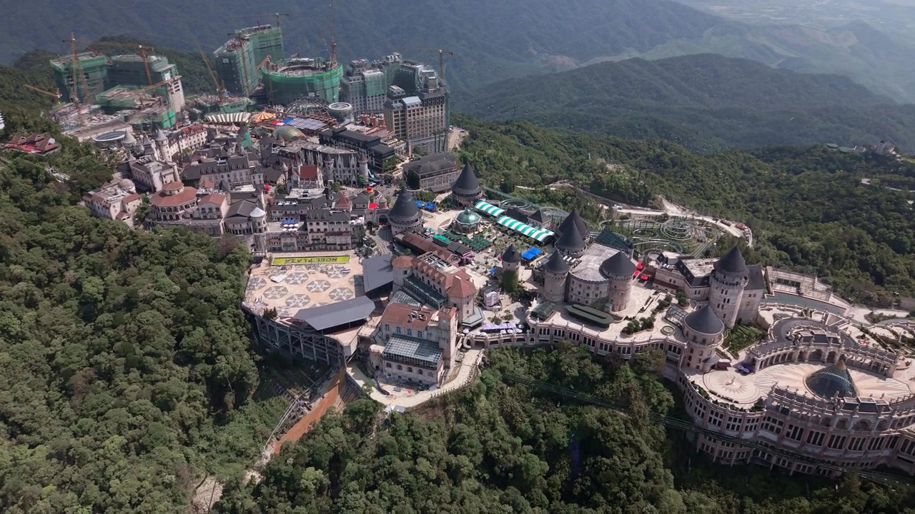 Vietnam'da drone ile yukarıdan çekilmiş, yemyeşil orman ve dağlık manzaraya yerleşmiş, kale benzeri mimariye sahip Ba Na Hills SunWorld tesisi.