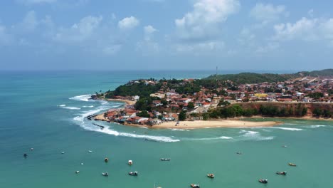 Incline-Hacia-Abajo-El-Plano-Aéreo-De-La-Playa-De-Cacimba-En-La-Ciudad-Costera-De-Baia-Formosa-En-Rio-Grande-Do-Norte,-Brasil-Con-Barcos-De-Pesca,-Casas-Costeras,-Pequeñas-Olas-Y-Aves-Marinas-Volando-Alrededor