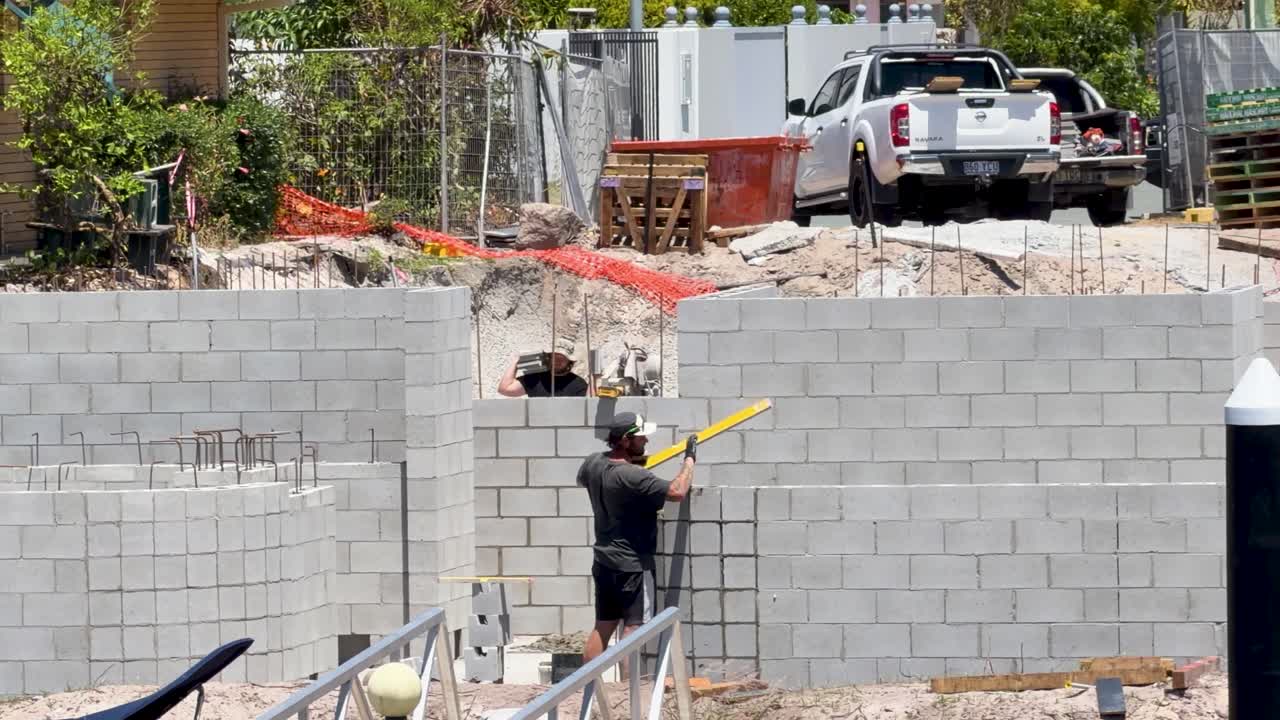 Worker uses spirit level to check alignment of concrete wall at residential construction site