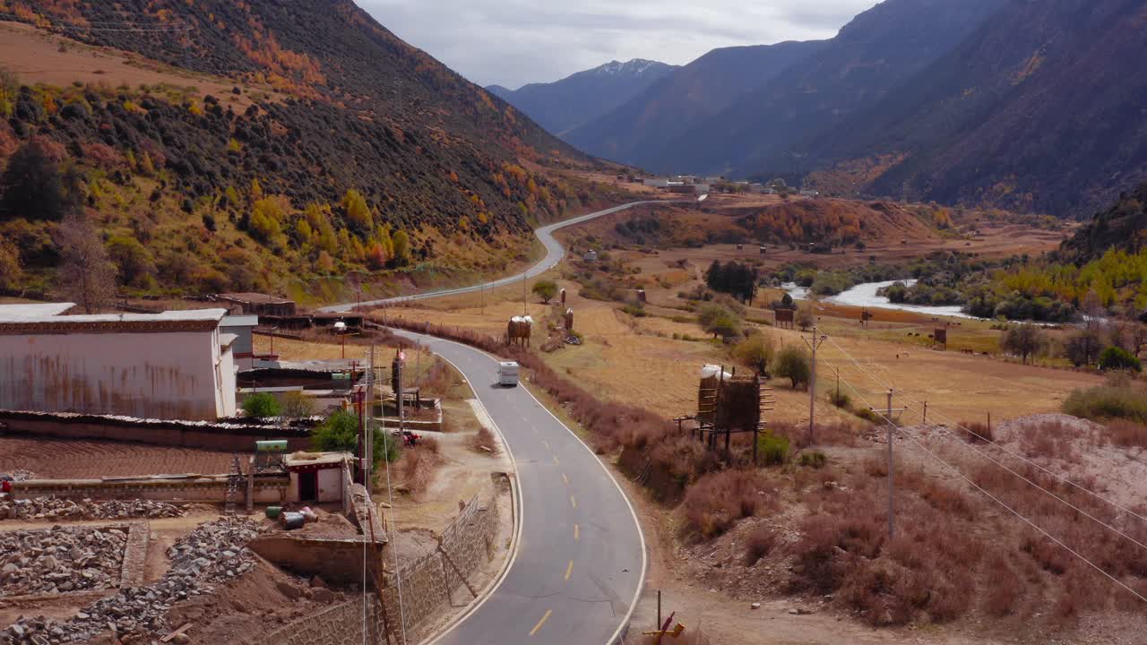 Campervan leaves Yading Valley villageentering autumn colored forest roadtrip adventure, aerial follow