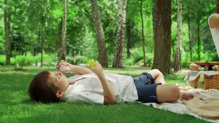 Bambino sdraiato su una coperta che soffia bolle di sapone nel parco