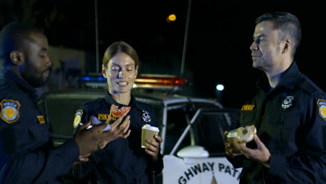 Policías-De-Razas-Mixtas,-Hombres-Y-Mujeres,-Hablando-Alegremente-Y-Tomando-Un-Descanso-Para-Patrullar-En-La-Calle-Por-La-Noche