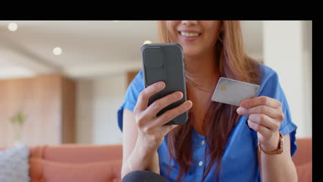holding smartphone and credit card, woman smiling while online shopping at home