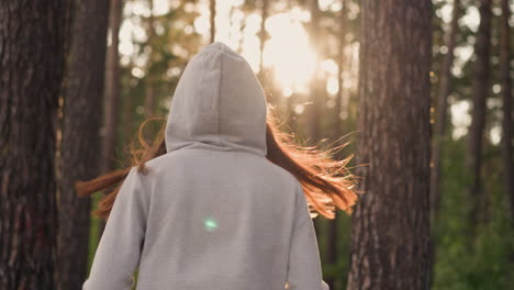 woman in hood jogging in forest. sun rays fall on lady athlete doing fitness against different types of trees. sunny weather and improved physical health