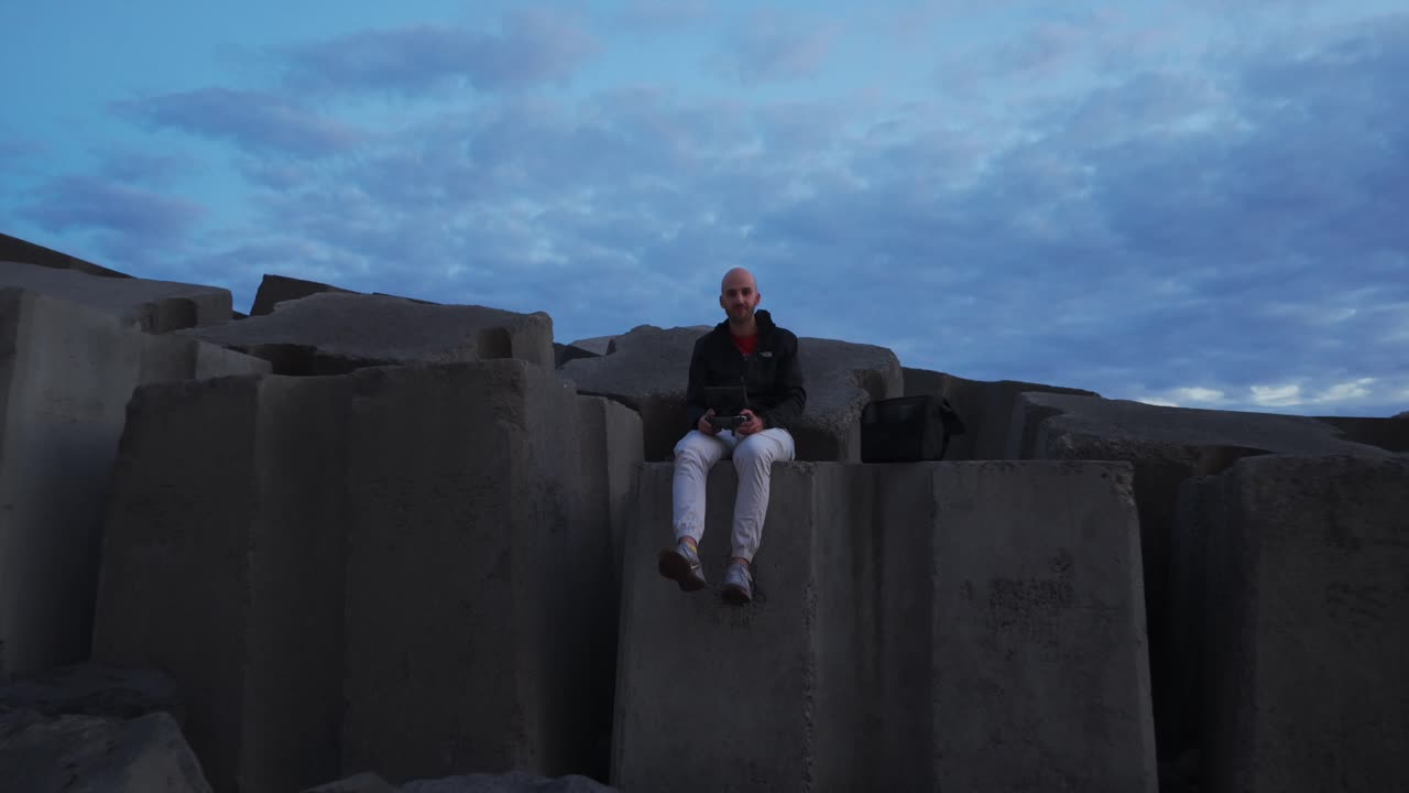 A Man Seated Over Seawall Rocks At The Marina In Calheta, Portugal. Aerial Pullback Shot