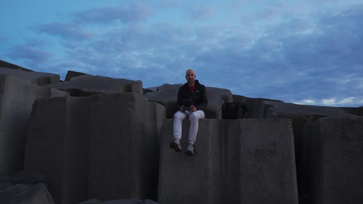 A Man Seated Over Seawall Rocks At The Marina In Calheta, Portugal. Aerial Pullback Shot