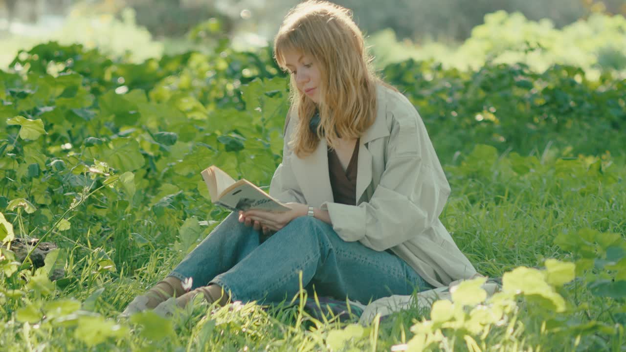 Tilt-down toward young lady sitting in lush park reading a book om summer sun
