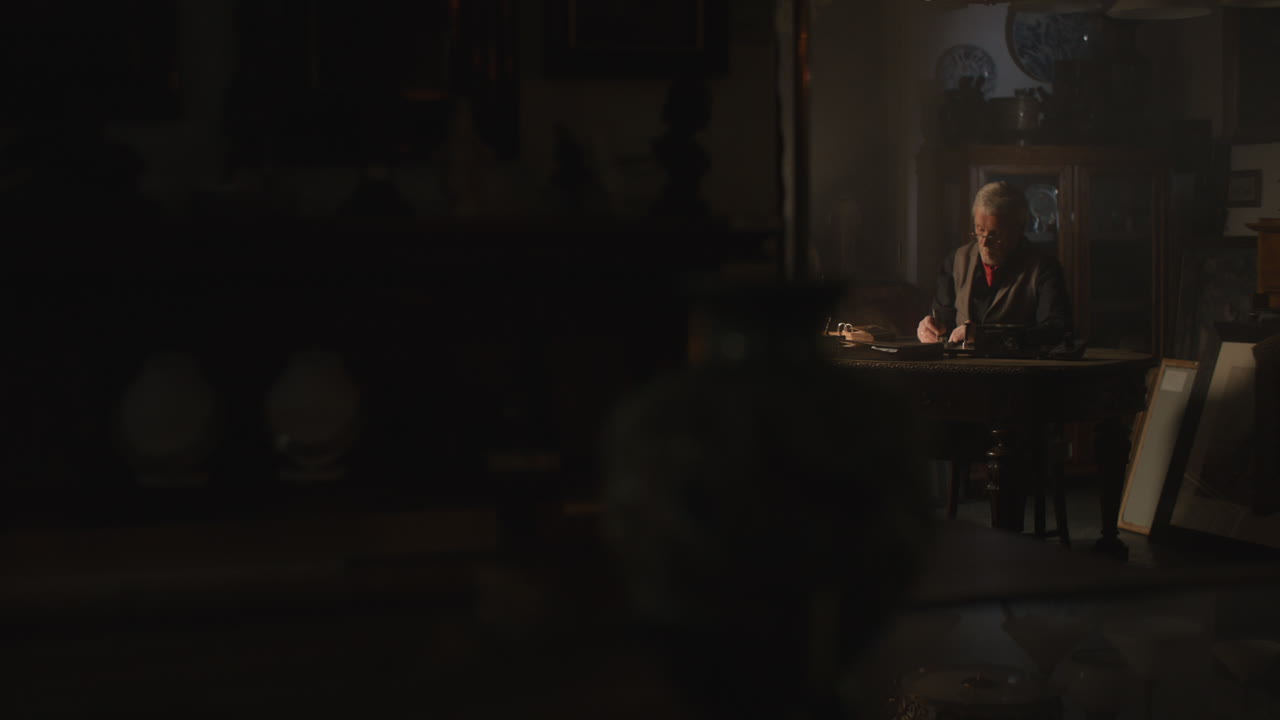 Old passionate man writes a letter in his office at night