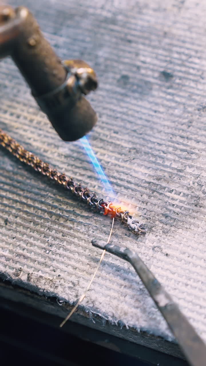 CU: experienced goldsmith welds links of decorative chain with metal string on fireproof asbestos sheet close view