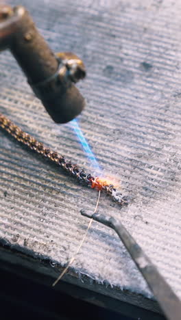 cu: experienced goldsmith welds links of decorative chain with metal string on fireproof asbestos sheet close view
