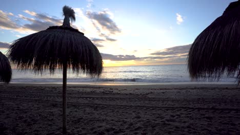 Marbella-beach-sun-umbrellas-panning-right-at-sunrise-over-the-Mediterranean-sea,-wide-angle-lens