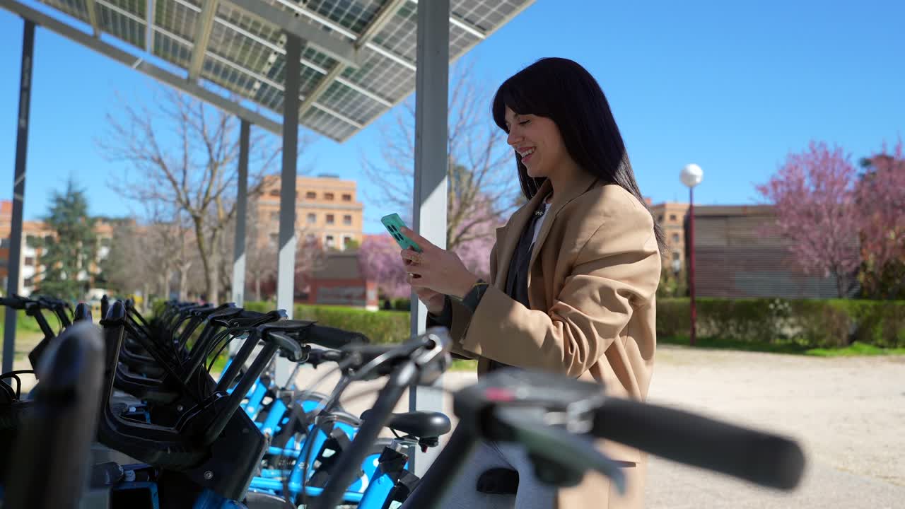 Young Woman Using Smartphone at Bike Sharing Station with Solar Panels