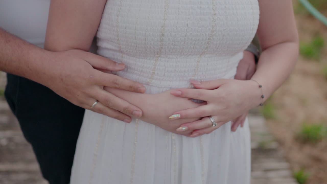 Close-up of a couple embracing, focusing on their intertwined hands and the woman's bracelet